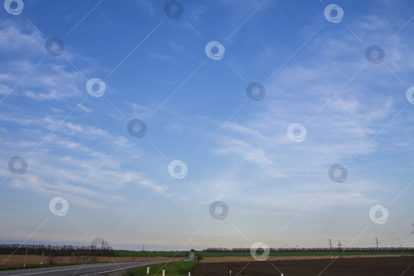 Скачать Голубое небо с мягкими облаками над асфальтированной дорогой, уходящей вдаль между сельскохозяйственными полями. Путешествие на автомобиле фотосток Ozero