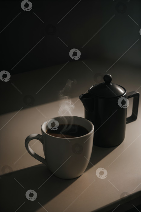 Скачать Дымящийся кофе в кружке с черным кофейником на белом столе фотосток Ozero