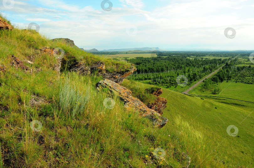 Скачать Вид со скалистой вершины высокого холма, поросшего травой, на плоскую долину с прямой гравийной дорогой. фотосток Ozero