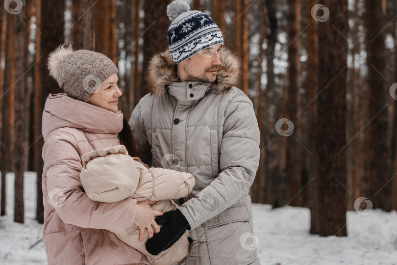 Скачать Стильная счастливая молодая семья гуляет с малышом по зимнему лесу, парку, семейное времяпрепровождение фотосток Ozero