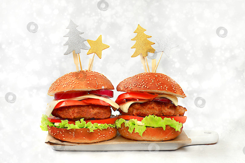 Скачать Два рождественских бургера с помидорами, оливками, сливочным сыром, луком, котлетами на праздничном столе с ярким боке, концепция новогодней еды. Реклама кафе, меню, визитная карточка ресторана, фотосток Ozero