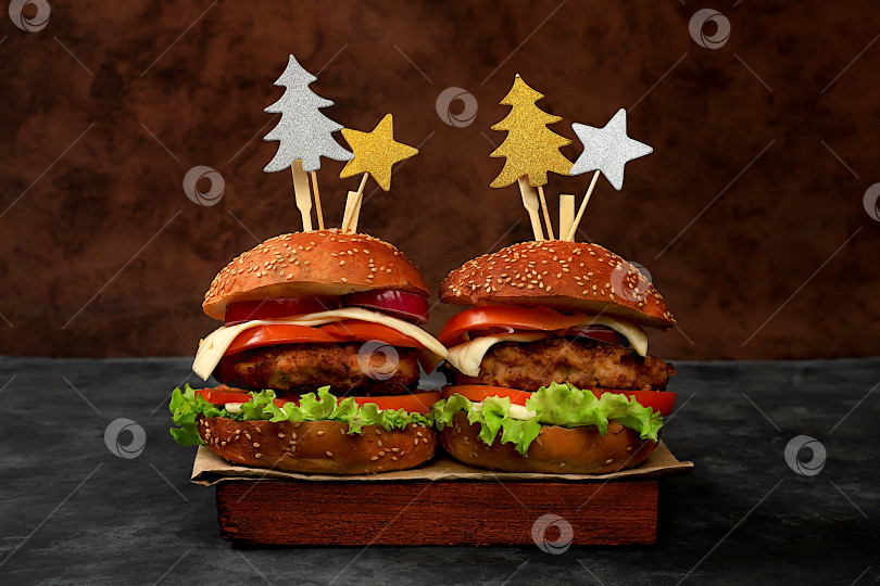 Скачать Два рождественских бургера с помидорами, оливками, сливочным сыром, луком, котлетами на праздничном темном столе, концепция новогодней еды. Реклама кафе, меню, визитная карточка ресторана, фотосток Ozero