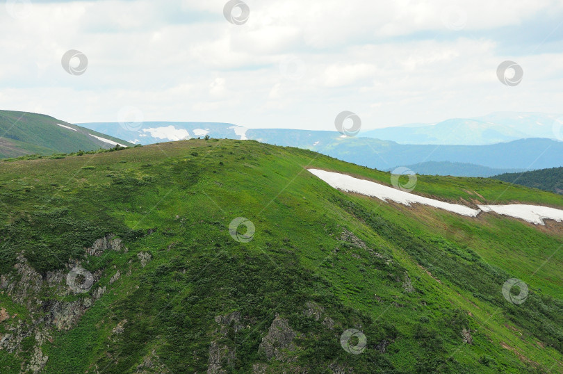 Скачать Высокий холм с травой и остатками снега под пасмурным летним небом. фотосток Ozero