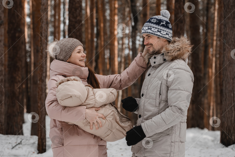 Скачать Стильная счастливая молодая семья гуляет с малышом по зимнему лесу, парку, семейное времяпрепровождение фотосток Ozero