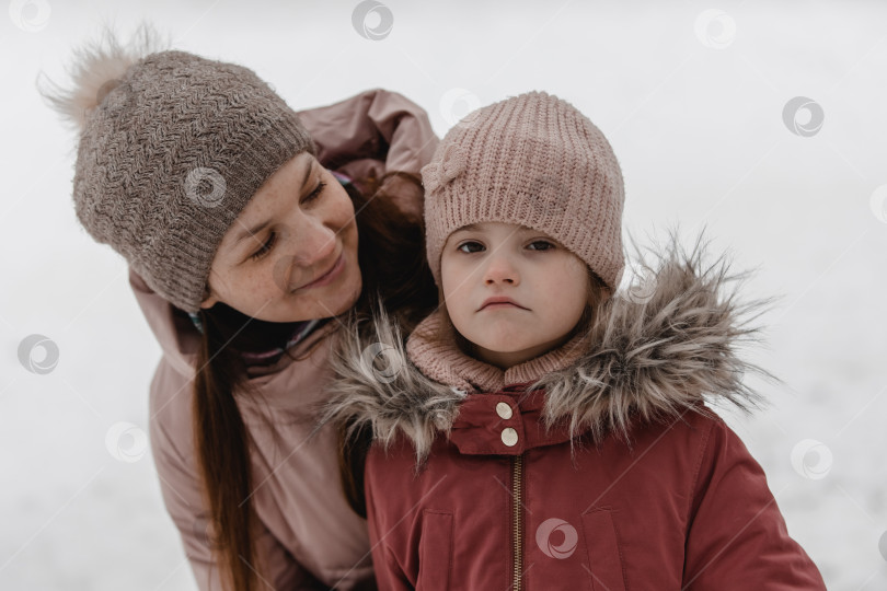 Скачать Семейная зимняя прогулка по лесу. Мать и дочь весело проводят время зимой в лесу в солнечную морозную погоду. Материнские объятия. фотосток Ozero