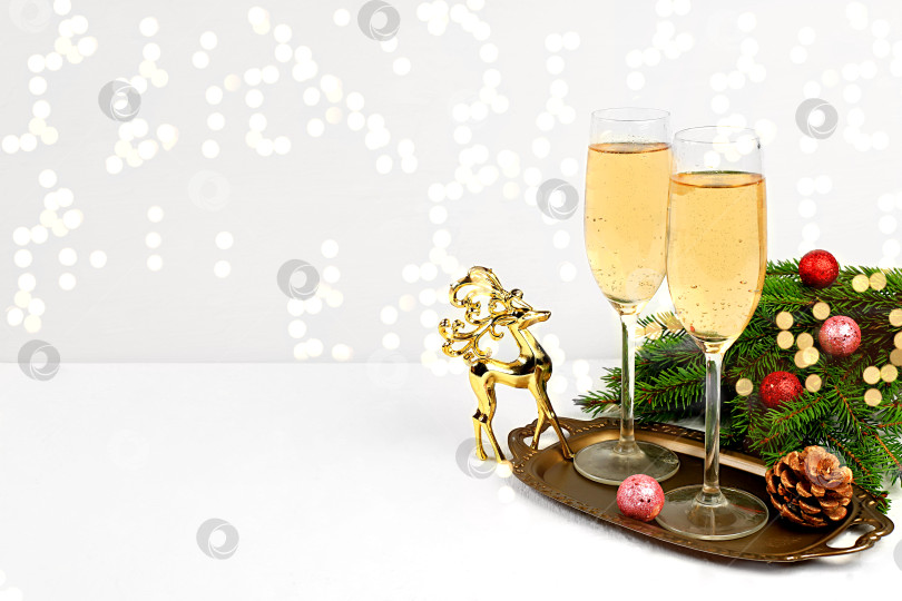 Скачать Два бокала шампанского на элегантном праздничном фоне с еловыми ветками и фигуркой оленя. Рождественский и новогодний макет для дизайна и демонстрации продукции, концепция Сочельника, фотосток Ozero