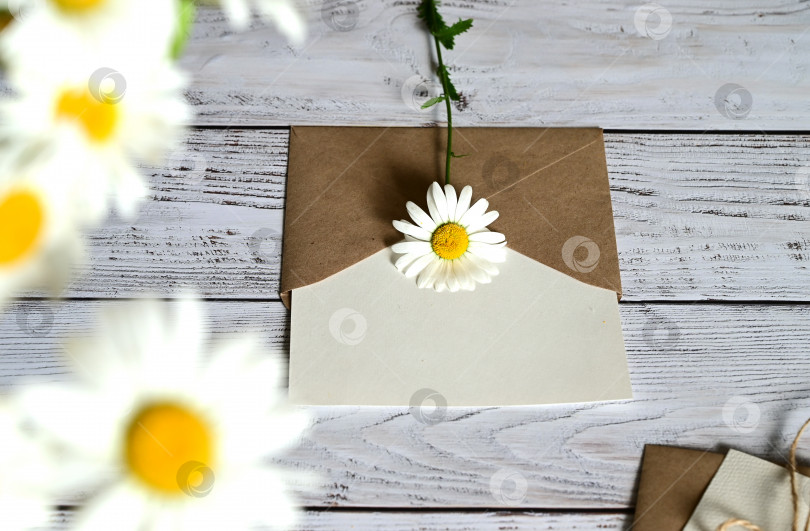Скачать Пустая поздравительная открытка с коричневым конвертом и белым цветком для мамы на деревянном столе в винтажном стиле и с виньетками фотосток Ozero