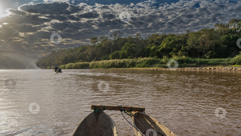Скачать Деревянные каноэ плывут по спокойной красно-коричневой реке. фотосток Ozero