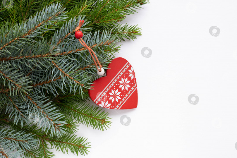 Скачать Зеленые и голубые еловые ветви с красным деревянным сердечком с белым орнаментом лежат на белом фоне. Место для вашего текста. Новогодняя концепция Рождества фотосток Ozero