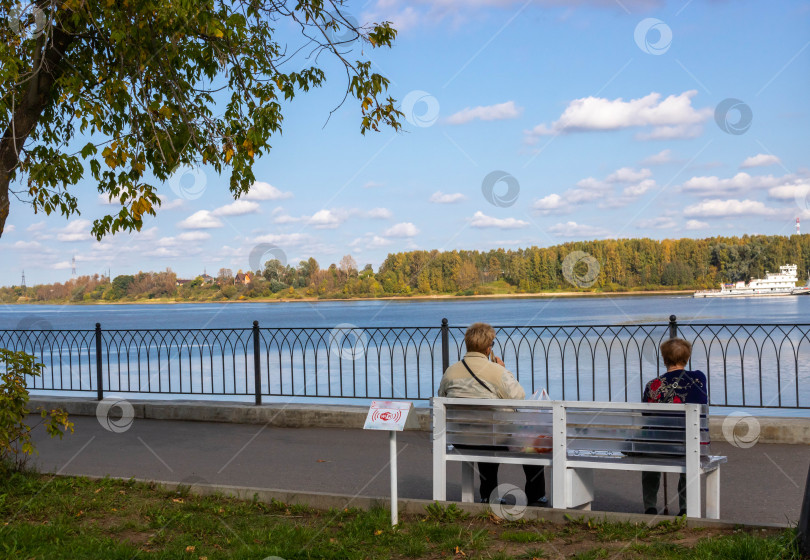 Скачать Две пожилые женщины сидят на скамейке у реки в городском парке. Расслабление. Концепция одиночества фотосток Ozero