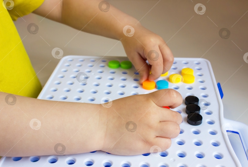 Скачать Ребенок играет и собирает детали мозаики на столе. Детские руки. фотосток Ozero