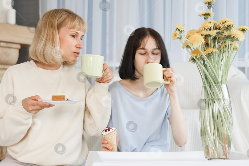 Скачать Мама и дочь-подросток едят десерт в гостиной дома, счастливая семья вместе. фотосток Ozero