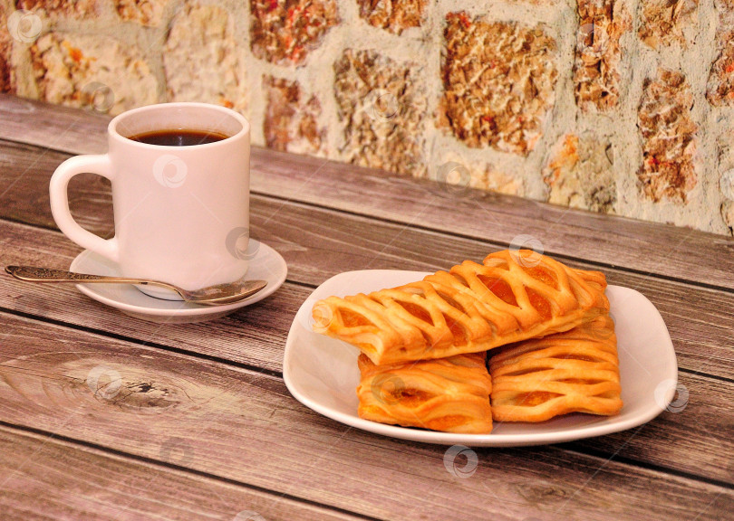 Скачать Чашка горячего черного кофе и тарелка с тремя слоеными булочками с фруктовым мармеладом на деревянном столе. фотосток Ozero