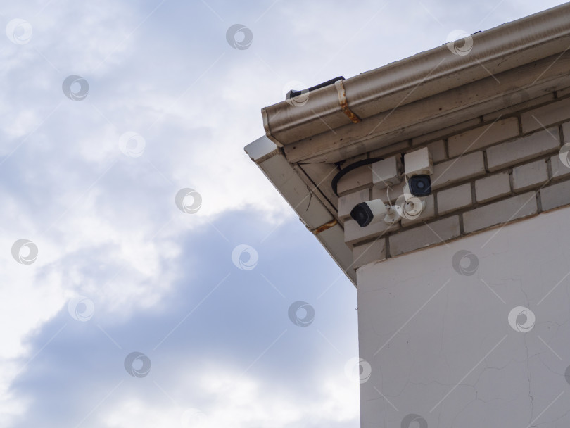 Скачать Камеры наружного наблюдения на старой стене под навесом крыши на фоне голубого неба. Наружное видеонаблюдение, камеры безопасности фотосток Ozero
