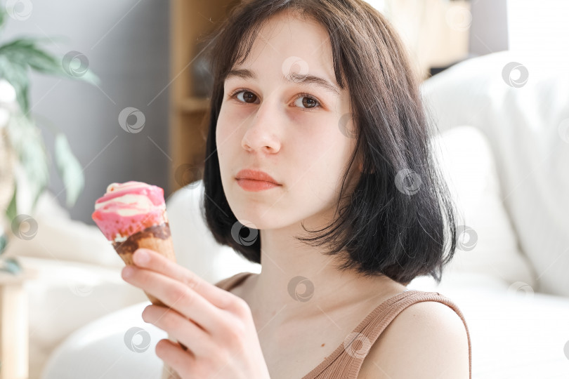 Скачать Девушка ест мороженое на фоне гостиной дома. Девочка-ребенок наслаждается едой и концепцией голода. фотосток Ozero