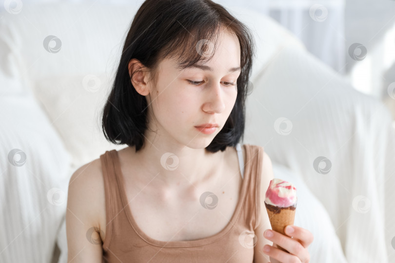 Скачать Девушка ест мороженое на фоне гостиной дома. Девочка-ребенок наслаждается едой и концепцией голода. фотосток Ozero