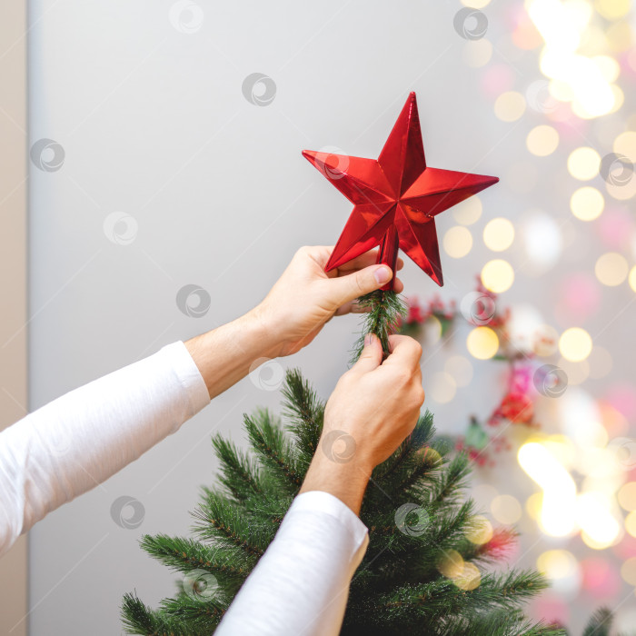 Скачать крупным планом мужские руки вешают рождественскую игрушку на рождественскую елку. боке и красная звезда фотосток Ozero