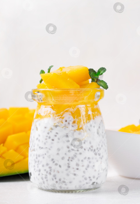 Скачать Пудинг из чиа с йогуртом и манго подается в стеклянной банке на белом столе. фотосток Ozero