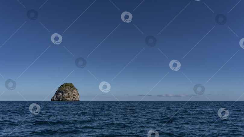 Скачать В голубом океане виден остров с крутыми скалистыми склонами. фотосток Ozero