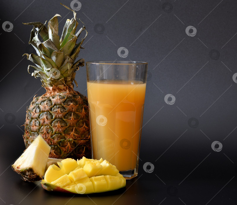 Скачать Высокий стакан со смесью сока манго и ананаса на черном фоне, рядом со спелыми фруктами. фотосток Ozero