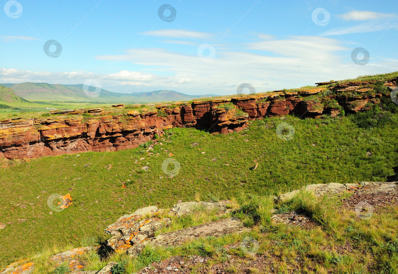 Скачать Широкие ряды каменных образований из красного песчаника тянутся вдоль пологих склонов высокого холма в солнечный летний день. фотосток Ozero