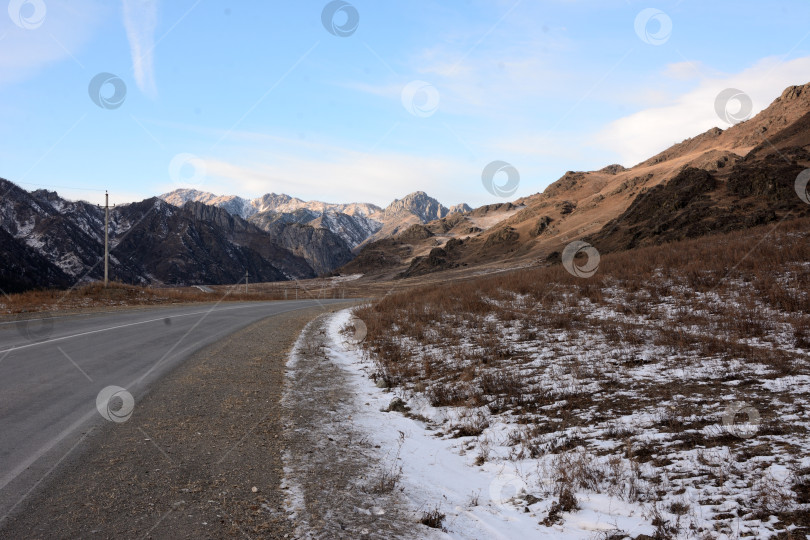 Скачать Правый поворот двухполосной асфальтированной дороги, проходящей через заснеженную долину, окруженную горами, в ясный зимний день. фотосток Ozero