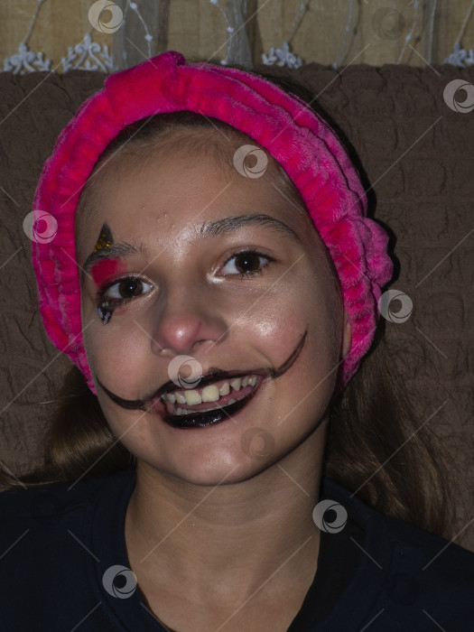 Скачать Девушка с ярким макияжем. Портрет крупным планом взволнованной улыбающейся девочки-подростка в ярком клоунском макияже для Хэллоуина, делающей селфи. Концепция праздничной вечеринки фотосток Ozero
