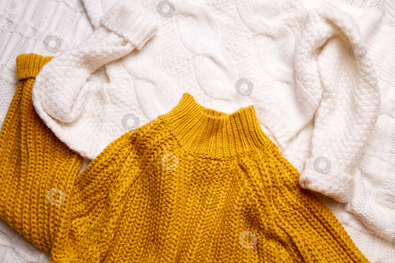 Скачать Белые и оранжевые вязаные свитера разбросаны по кровати. фотосток Ozero