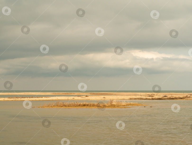 Скачать Вид на неглубокую лагуну, отделенную от моря пологим песчаным пляжем ранней весной в солнечный день. Желтые ракушки- песчаные острова в морской воде фотосток Ozero