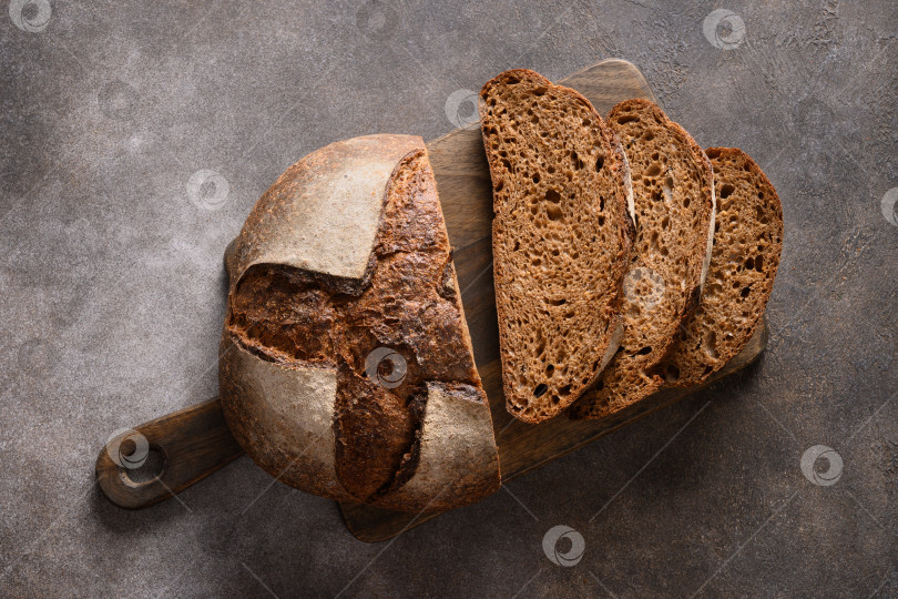 Скачать Буханка свежеиспеченного хлеба на закваске из конопляной муки на разделочной доске. Домашний хлеб с семечками на сером фоне. фотосток Ozero