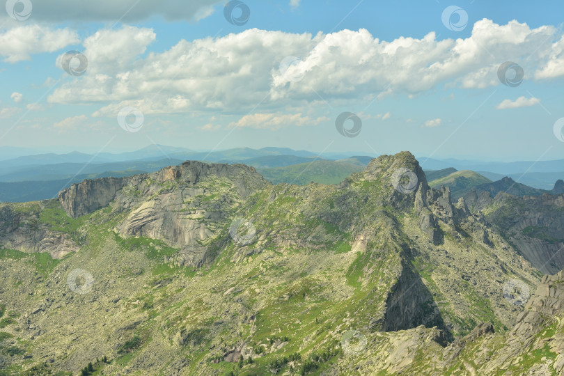 Скачать Высокий скалистый массив с остроконечными вершинами, частично поросшими травой, под пасмурным летним небом. фотосток Ozero