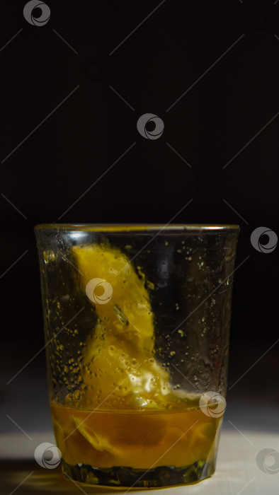 Скачать Ломтики лимона, залитые медом, в стеклянном бокале. Ломтики лимона с медом к чаю в стакане на деревянной поверхности на темном фоне фотосток Ozero