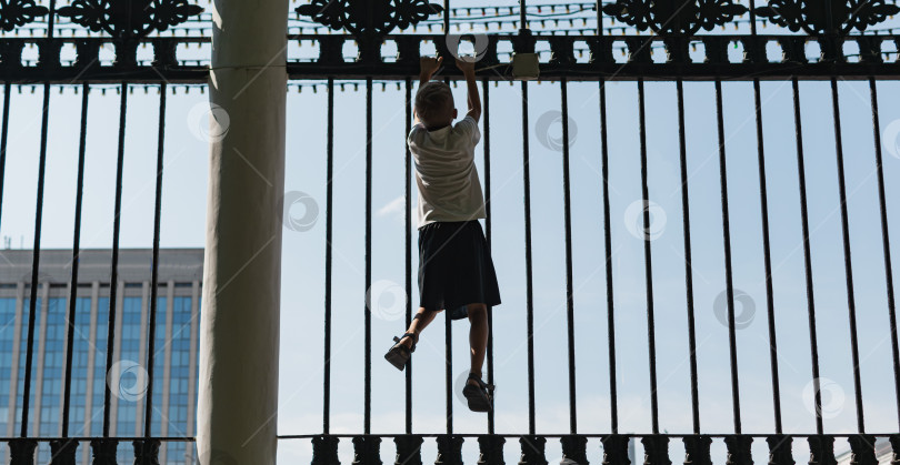 Скачать Маленький мальчик пытается перелезть через забор фотосток Ozero