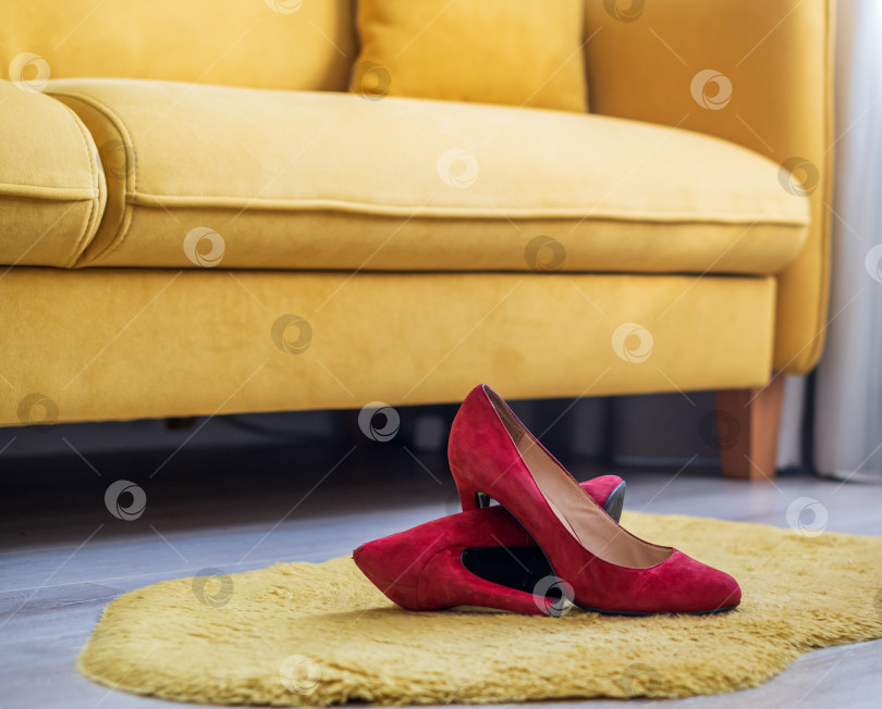 Скачать красные женские туфли на высоком каблуке лежат на полу в комнате рядом с желтым диваном фотосток Ozero