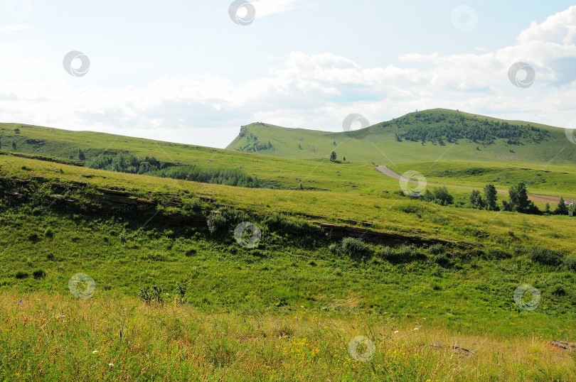 Скачать Грунтовая дорога, идущая по пологим склонам высоких холмов под ясным летним небом в живописной долине. фотосток Ozero