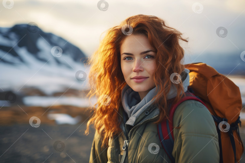 Скачать Улыбающаяся рыжеволосая женщина-путешественница в верхней одежде и с рюкзаком в походе по северу смотрит в камеру на открытом воздухе фотосток Ozero
