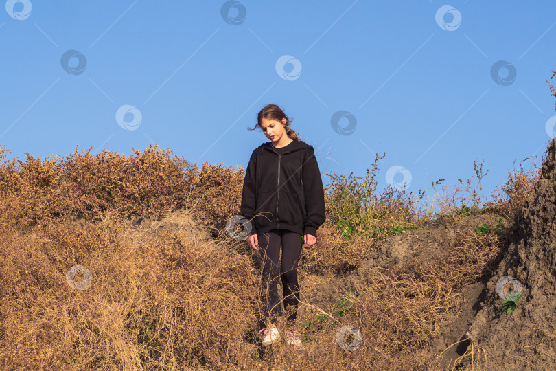 Скачать Девочка-подросток спускается по крутому склону холма, заросшему высохшей желтой травой фотосток Ozero