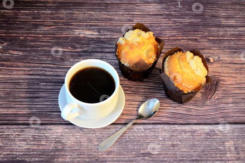 Скачать Чашка горячего черного кофе и две свежие булочки в бумажной обертке на деревянном столе. фотосток Ozero