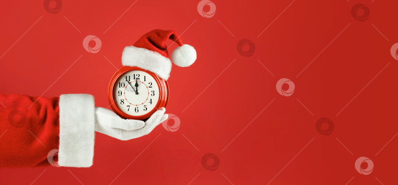 Скачать Рука Деда Мороза держит красный будильник в новогодней шапочке фотосток Ozero