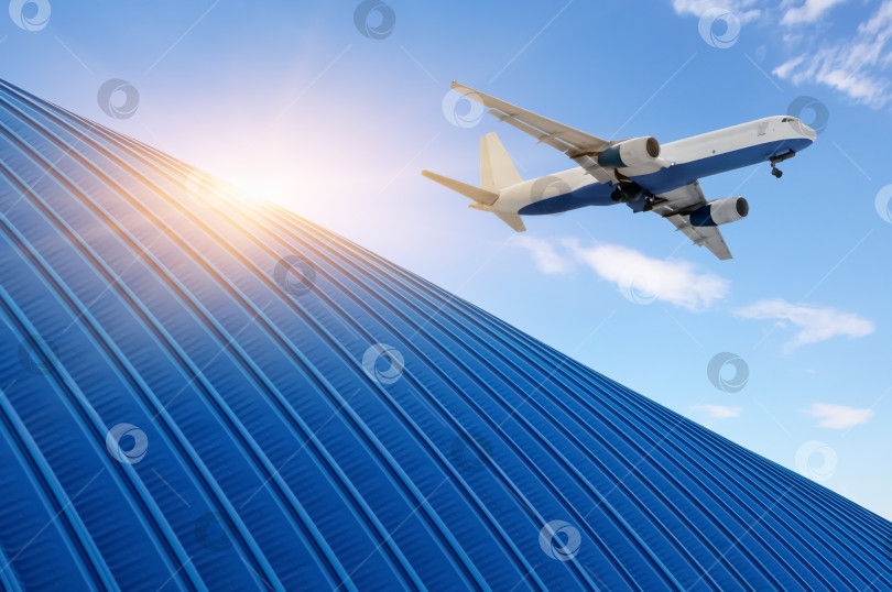 Скачать Грузовой самолет пролетает над крышей ангара склада в лучах яркого солнца. Управление логистической цепочкой поставок и концепция международного экспорта товаров. фотосток Ozero