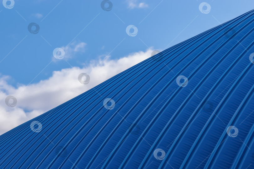 Скачать Фрагмент ангара из синего металлопроката на фоне неба с облаками. Простая металлическая конструкция промышленного здания снаружи фотосток Ozero