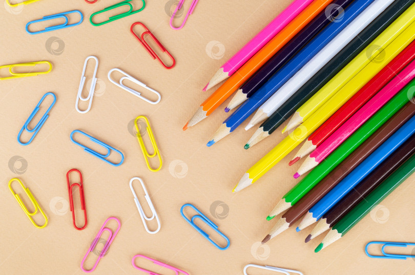 Скачать Множество разноцветных карандашей и скрепок для бумаги на приятном бежевом фоне фотосток Ozero