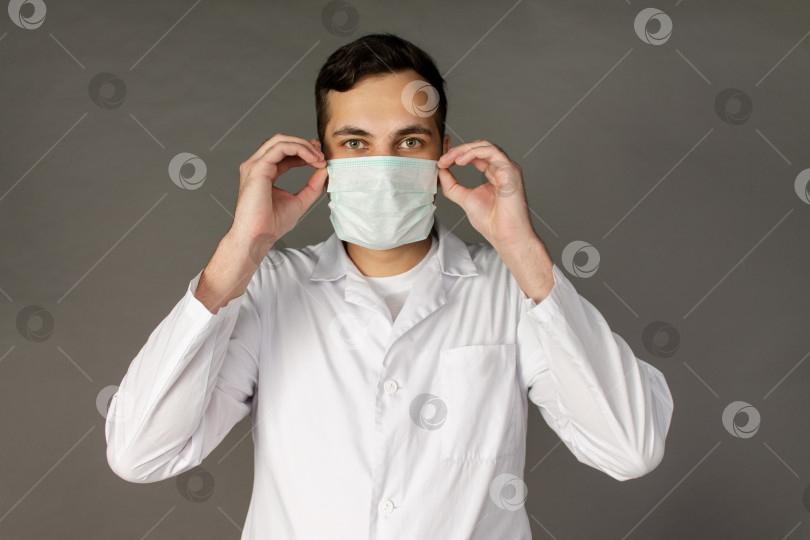 Скачать Врач держит и надевает медицинскую маску, чтобы защитить себя от нового вируса - коронавируса фотосток Ozero