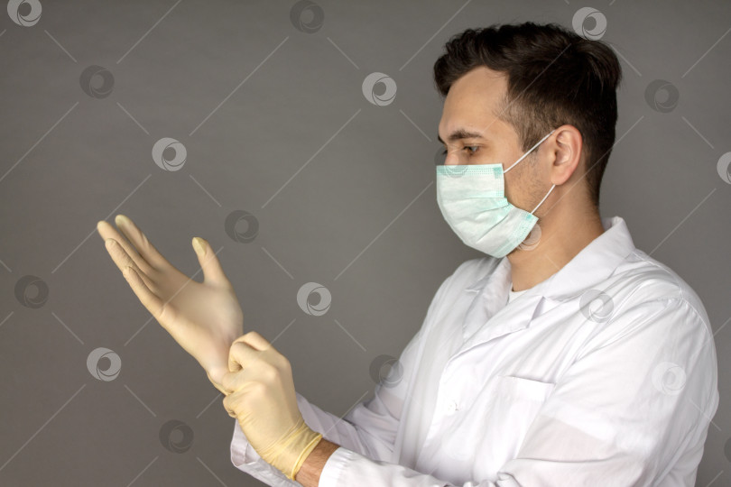 Скачать Портрет врача в медицинском халате, надевающего перчатки перед проведением тестов на коронавирус фотосток Ozero