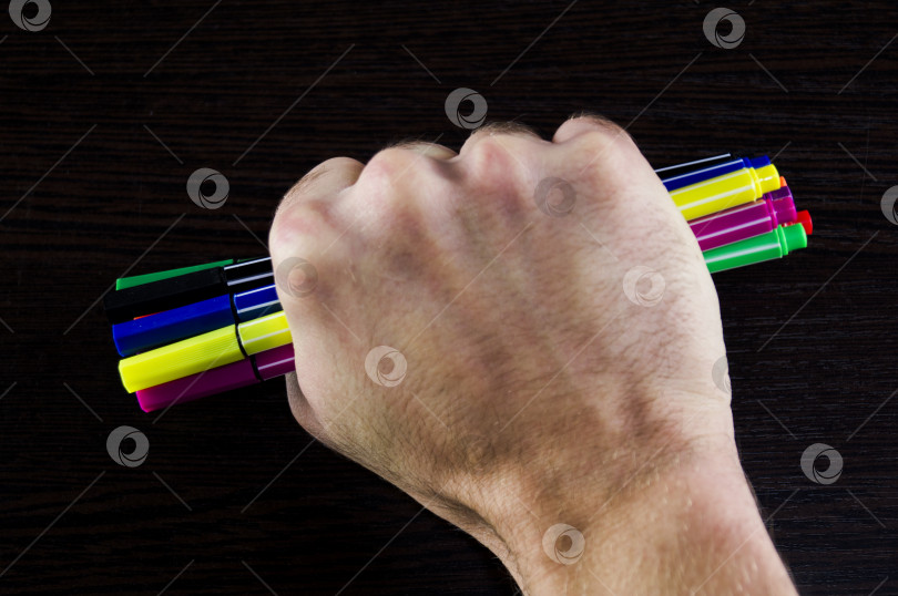 Скачать Разноцветные маркеры в руке на темном фоне стола фотосток Ozero