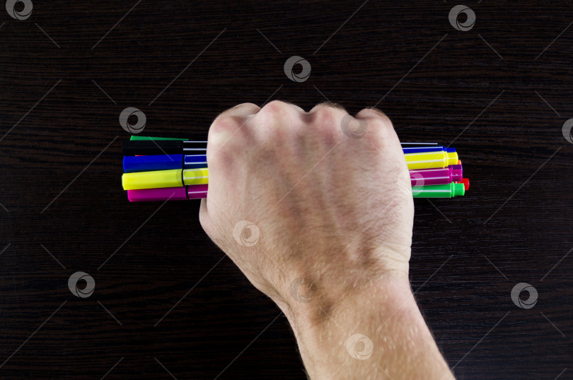 Скачать Разноцветные маркеры в руке на темном фоне стола фотосток Ozero