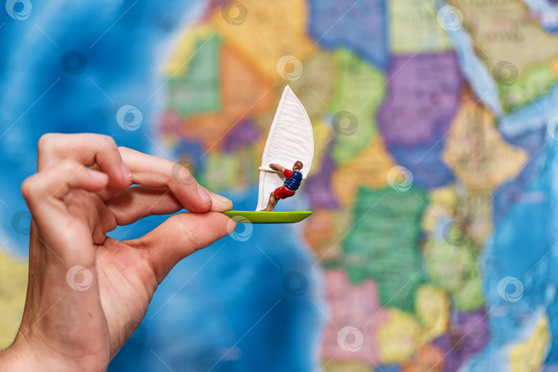 Скачать Детская рука держит игрушечный виндсерфер на фоне карты мира фотосток Ozero
