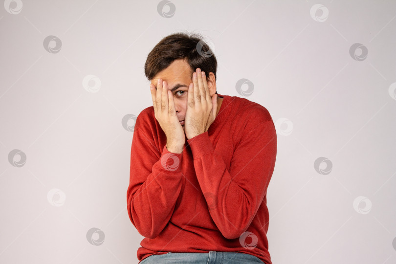 Скачать Молодой человек в красном свитере закрывает лицо руками фотосток Ozero