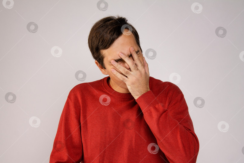 Скачать Молодой человек в красном свитере закрывает лицо руками фотосток Ozero