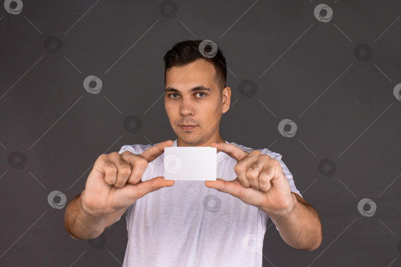 Скачать Молодой человек в белой футболке держит в руках визитную карточку фотосток Ozero